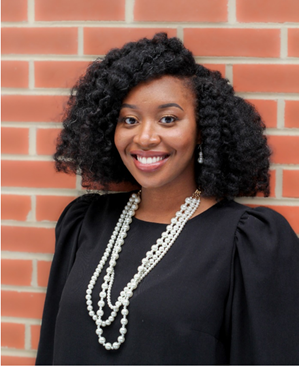 A person smiling in front of a brick wall  Description automatically generated
